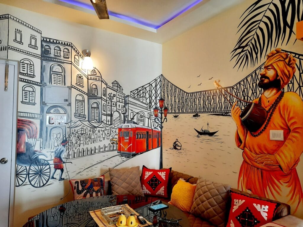 Hand-painted Kolkata city mural featuring Howrah Bridge, tram, rickshaw, and cultural figure wall art in a modern living room.